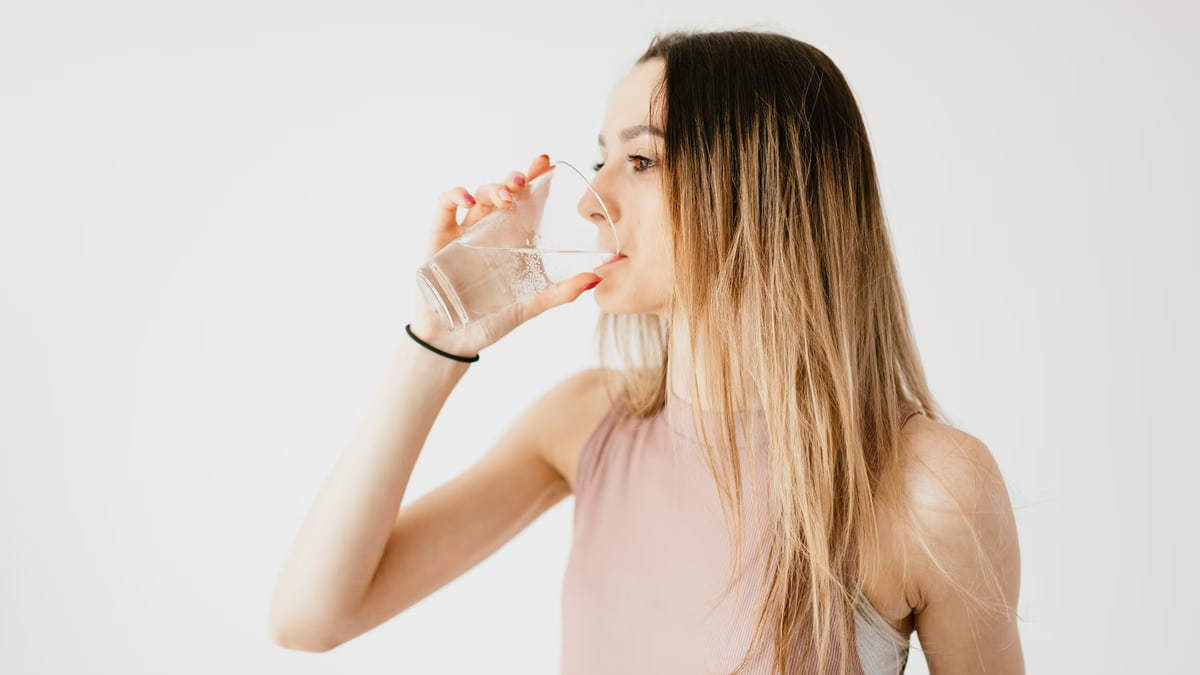 Young thirsty fit female with long hair in sportswear drinking water while recreating after workout